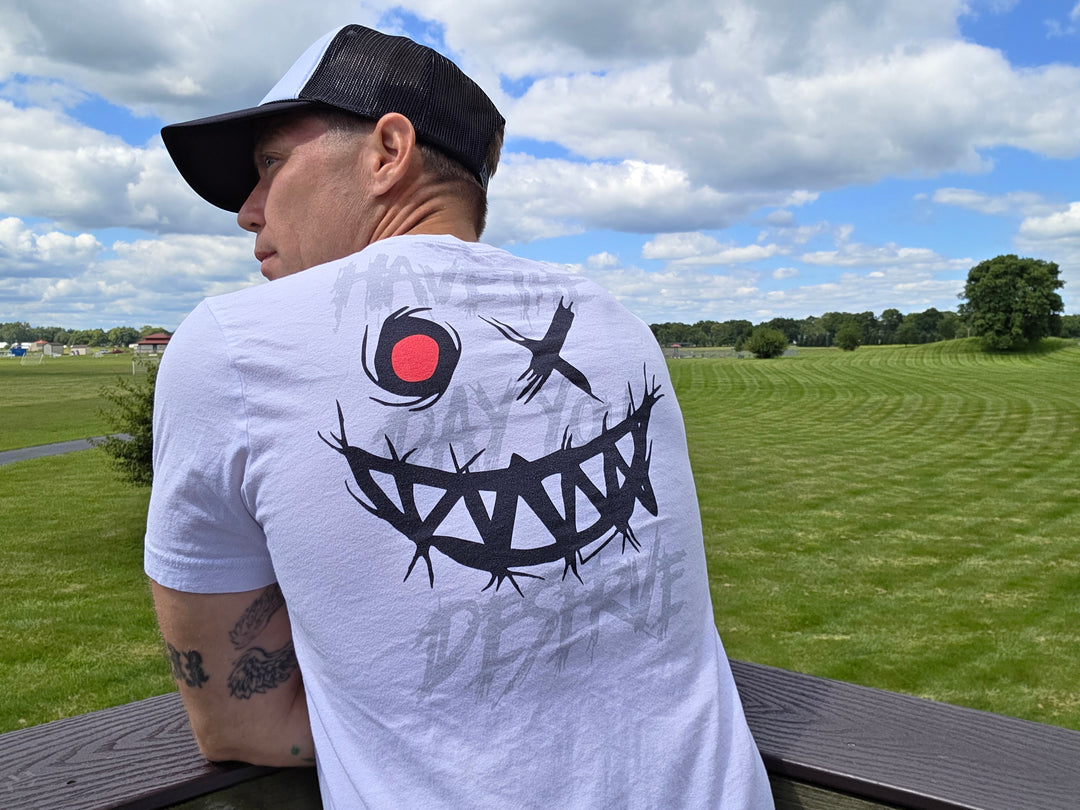 An urban man at a park is wearing the Evil Grin And Slogan Graphic Tee, back view.