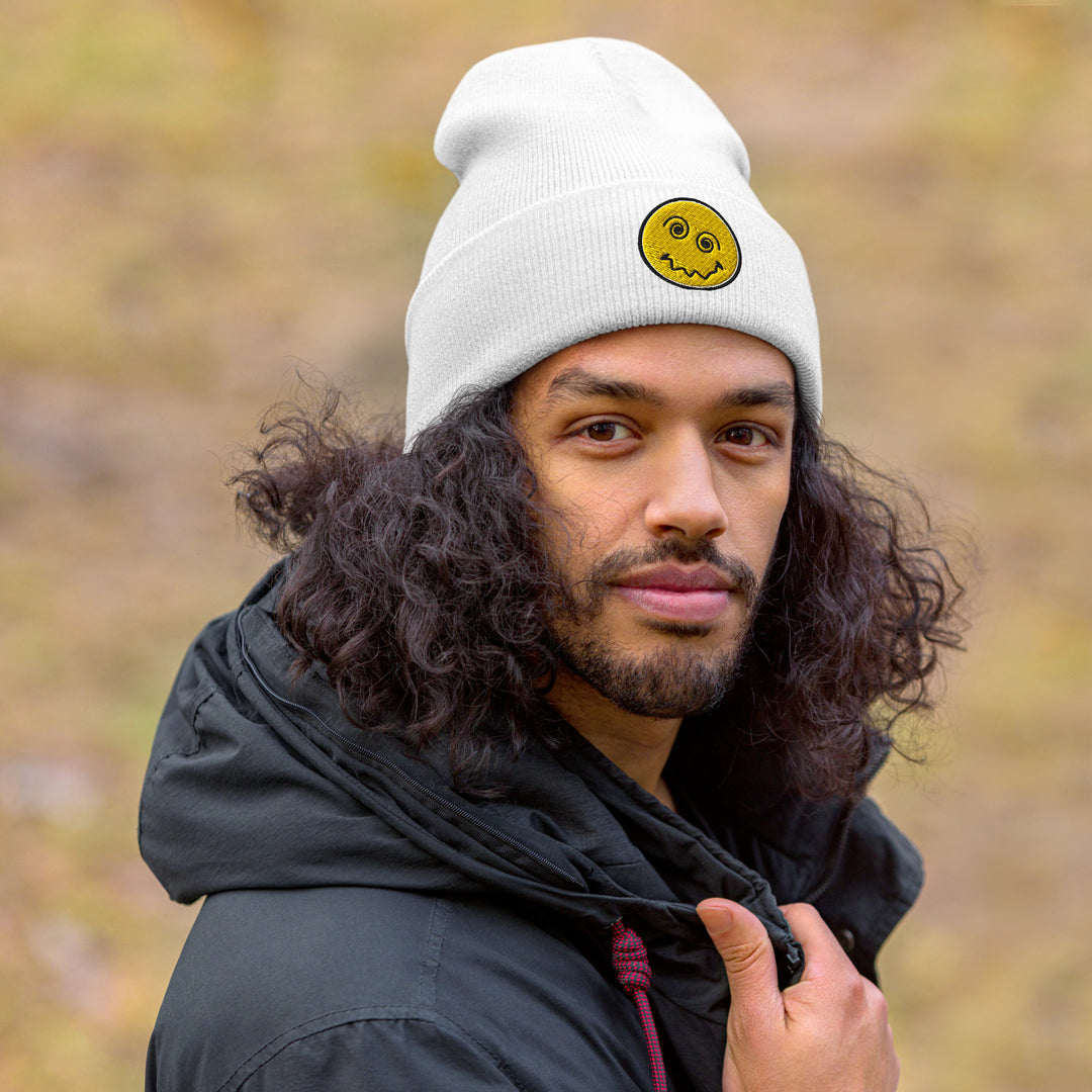 An urban man is outside wearing the Embroidered Anxiety Face Cuffed Beanie, front view.